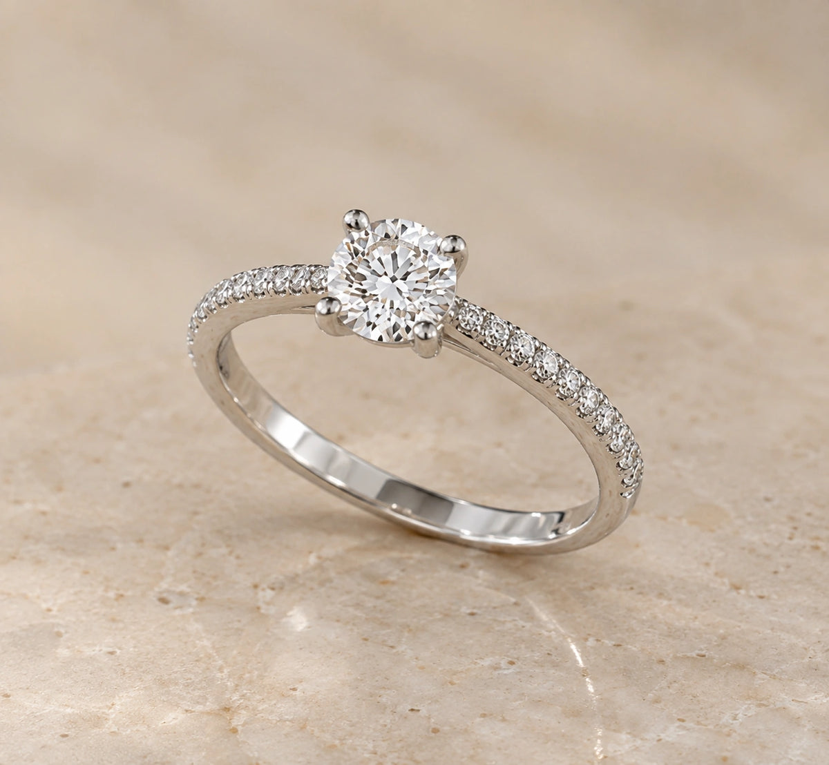 Close-up of a round brilliant diamond solitaire in 14K white gold with pavé diamonds on the shoulders