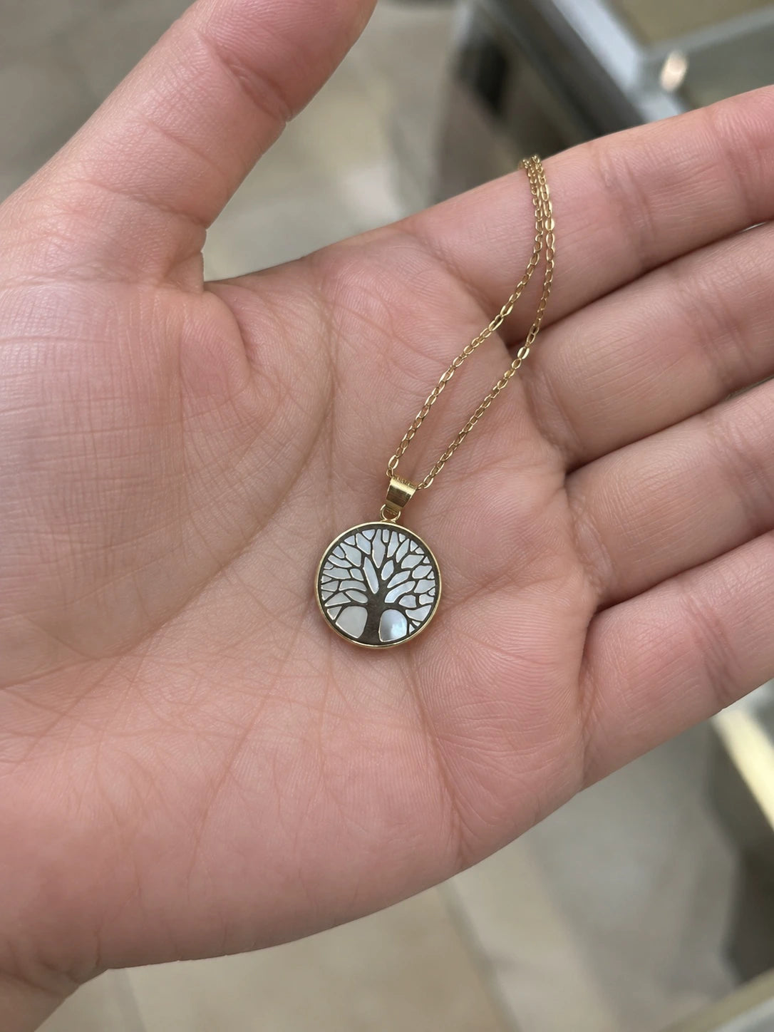14K yellow gold Tree of Life pendant necklace held in a hand to show its size