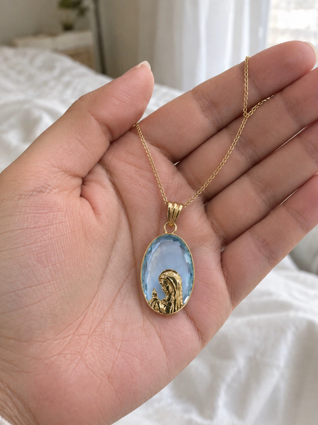 Light blue stone Virgin Mary pendant necklace in 14K gold held in a hand to show its size