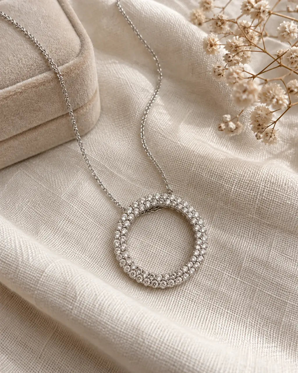 Diamond circle pendant on a white gold chain lying on cream linen