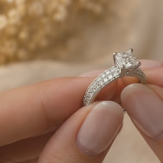 Hand holding and turning the princess cut diamond engagement ring with domed pavé band in 14K white gold