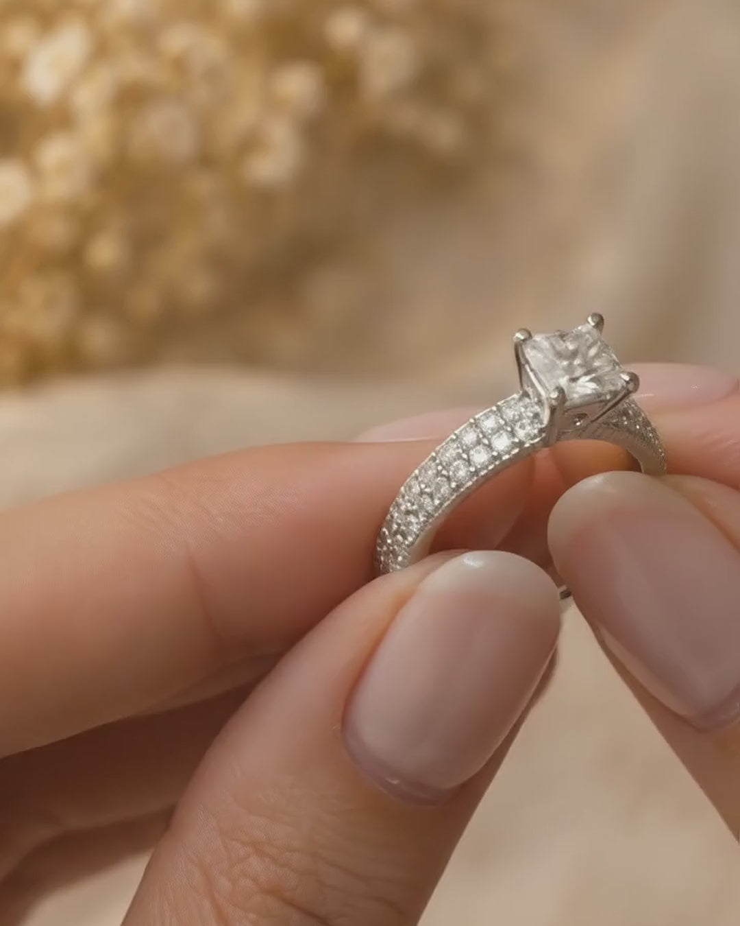 Hand holding and turning the princess cut diamond engagement ring with domed pavé band in 14K white gold