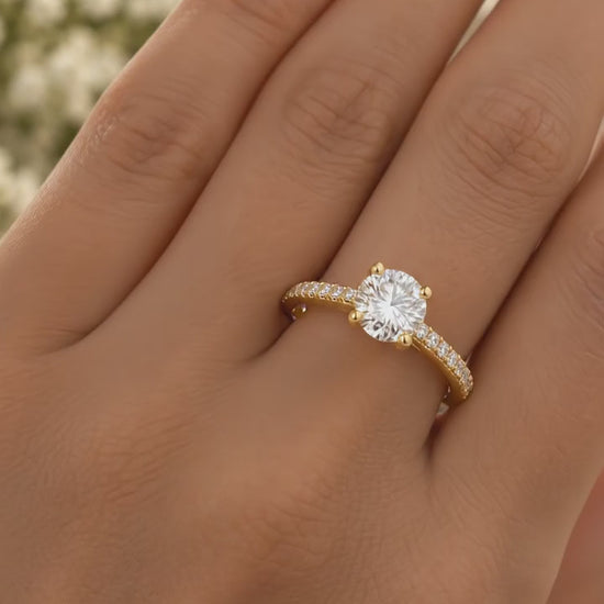 Round solitaire engagement ring in 14K yellow gold with a pavé diamond band, worn on a hand
