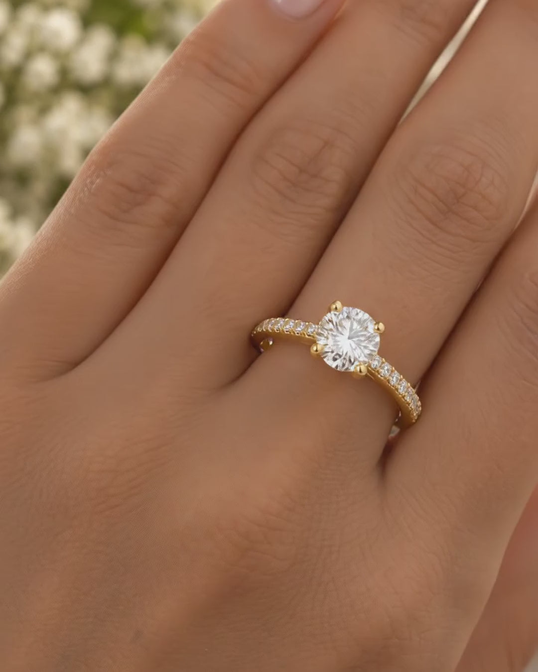Round solitaire engagement ring in 14K yellow gold with a pavé diamond band, worn on a hand