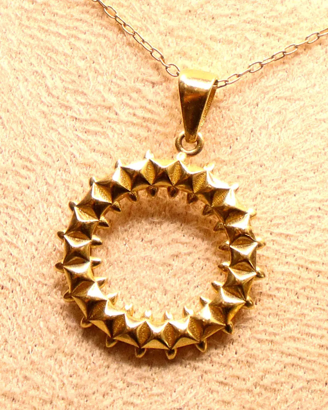 Close-up of the 14K gold sunburst circle pendant: hand-finished pyramid studs and polished bail