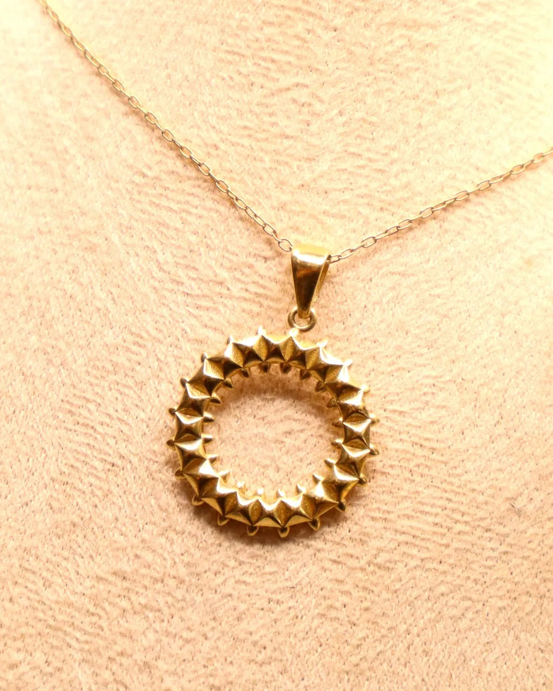 Sunburst circle pendant necklace in 14K yellow gold, ring of pyramid studs on a fine chain, on a beige bust