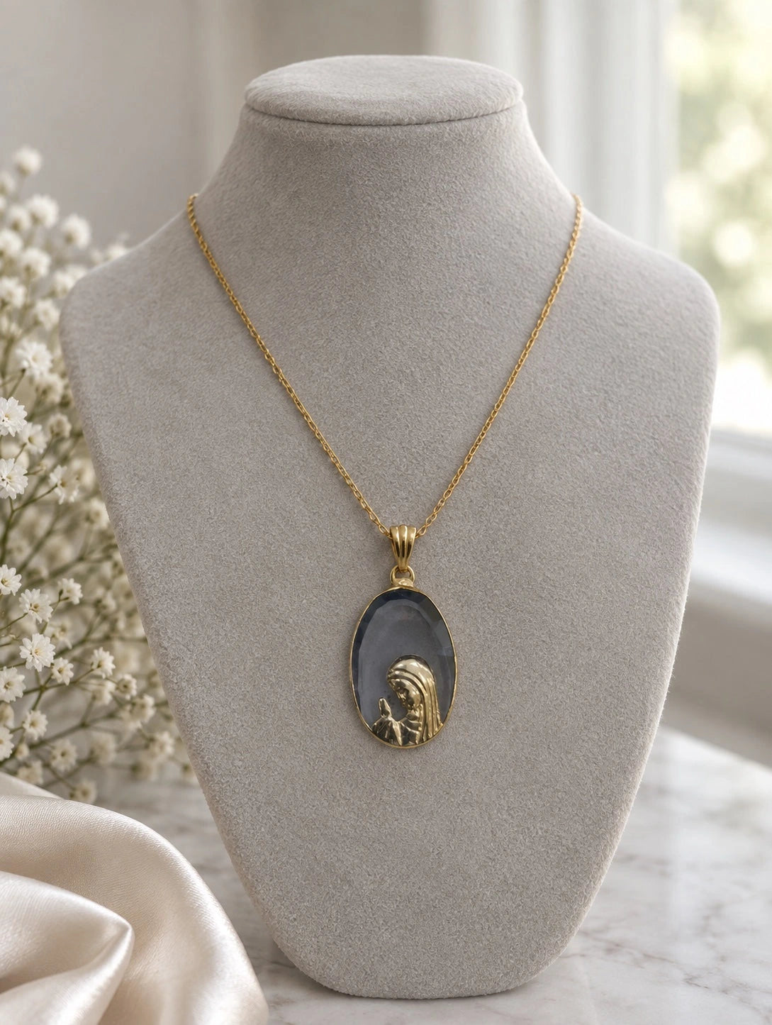 Dark stone Virgin Mary pendant necklace in 14K gold on a jewelry bust