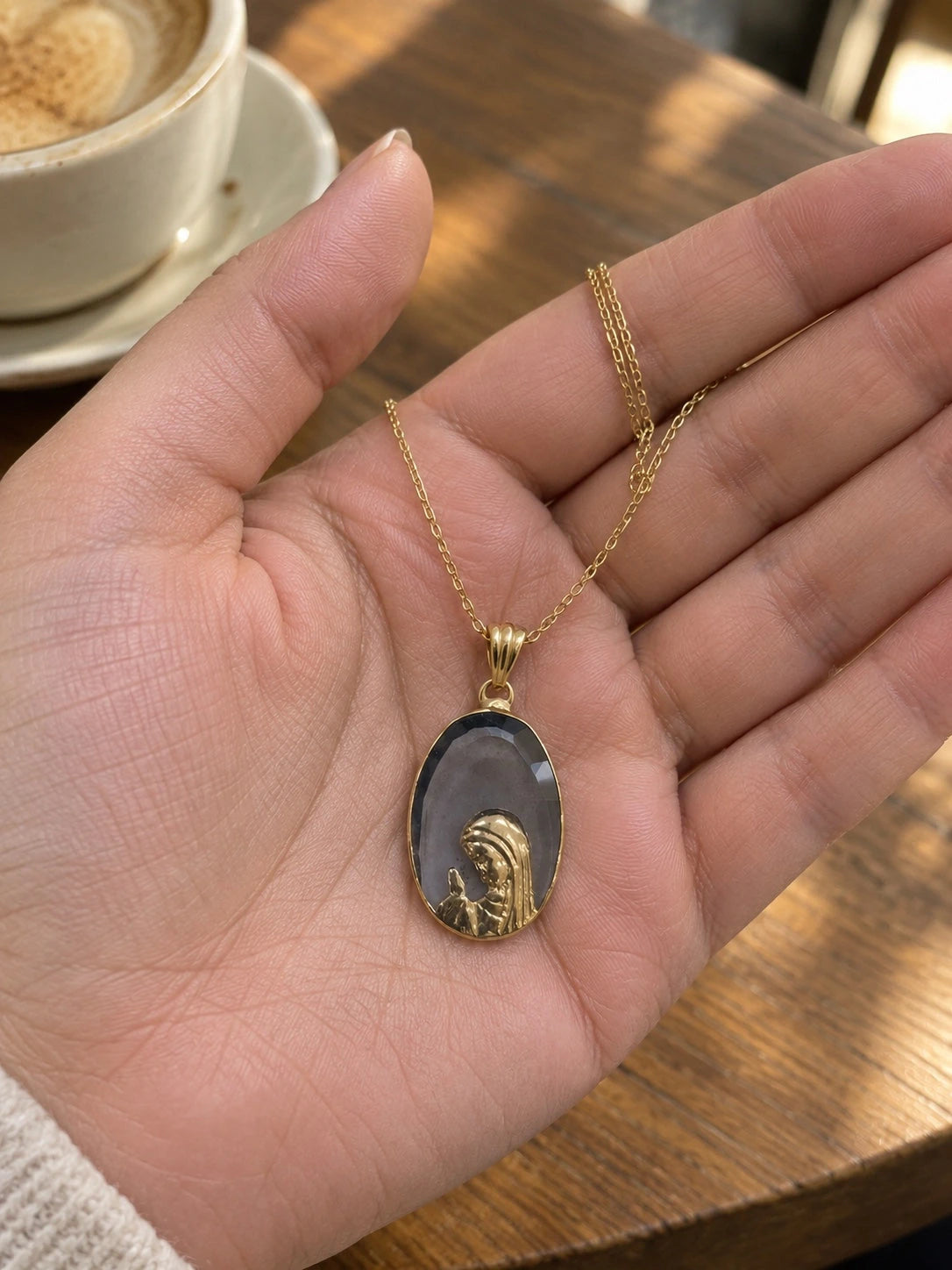 Dark stone Virgin Mary pendant necklace in 14K gold held in a hand to show its size