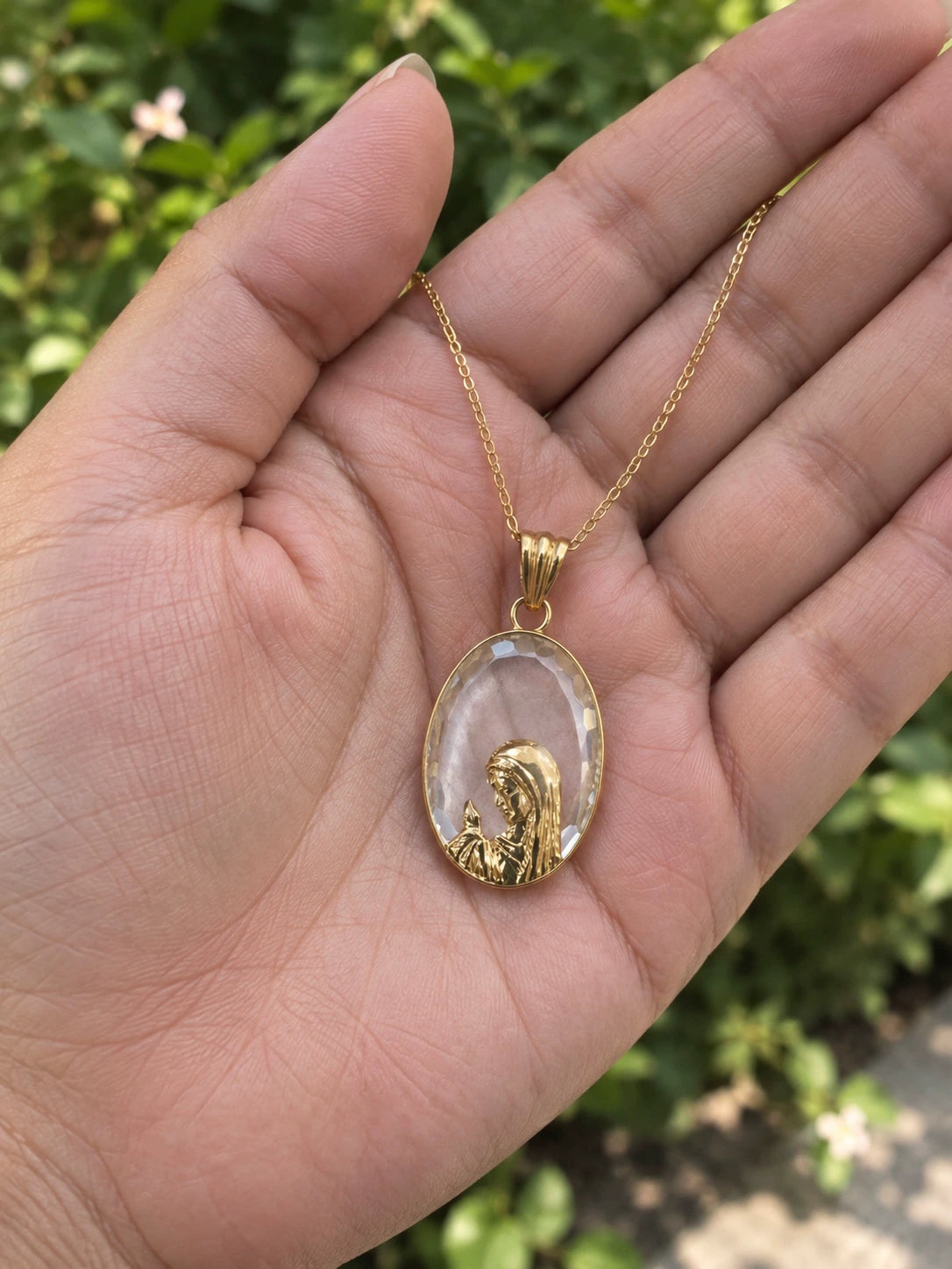 Clear stone Virgin Mary pendant necklace in 14K gold held in a hand to show its size