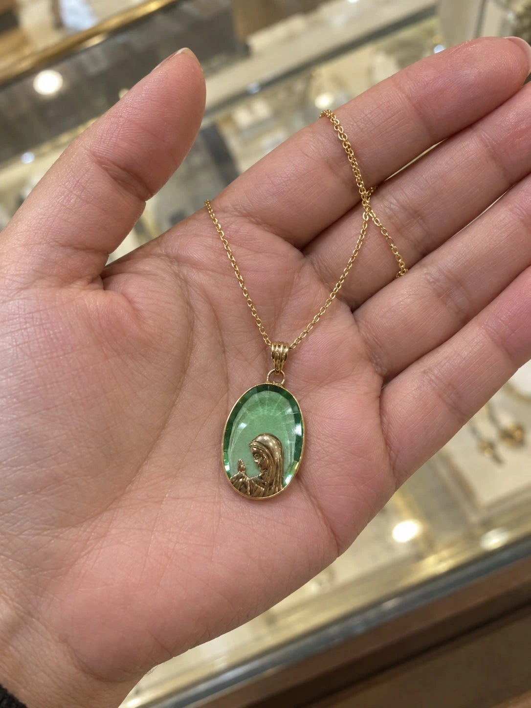 Green stone Virgin Mary pendant necklace in 14K gold held in a hand to show its size