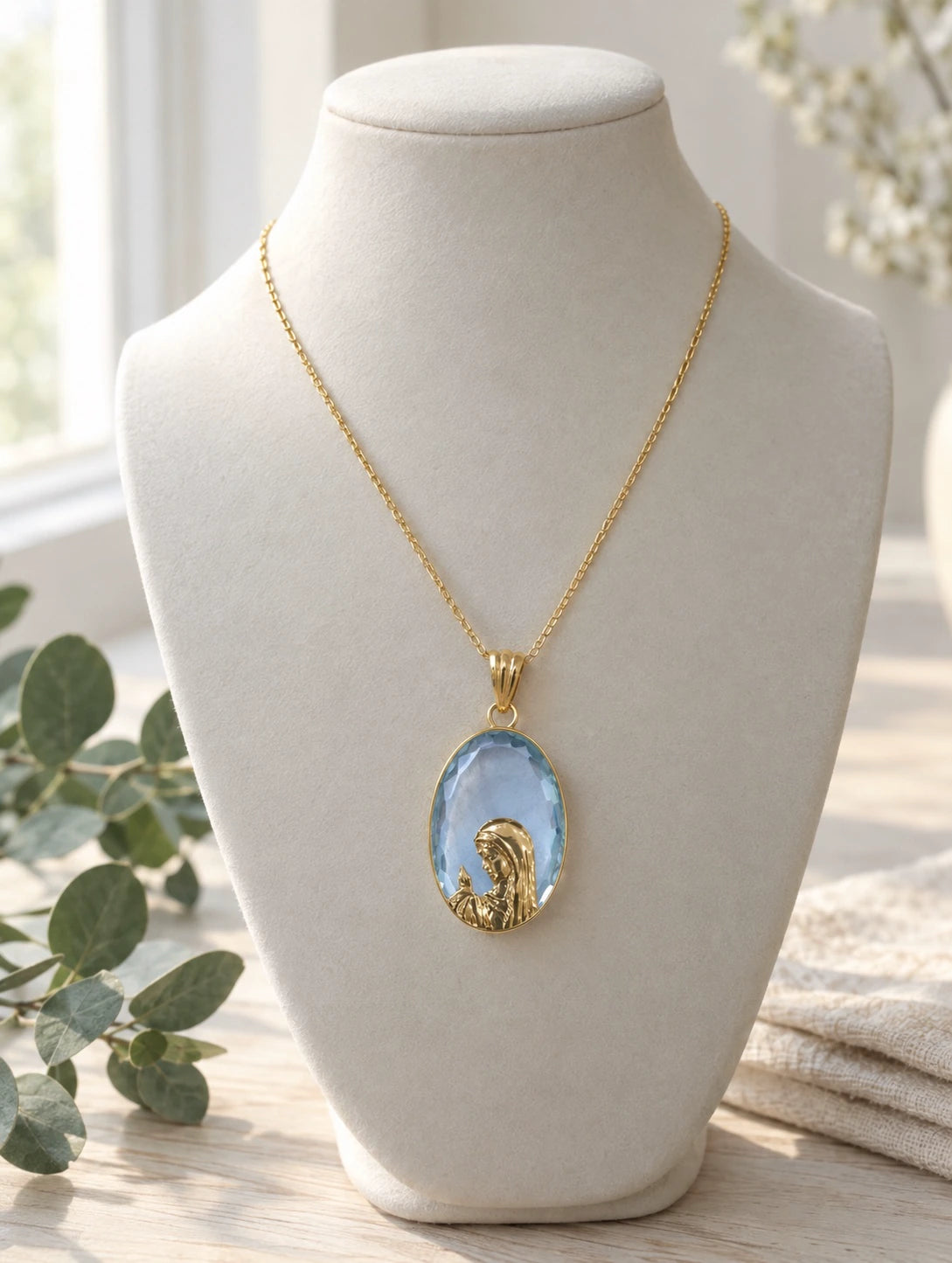 Light blue stone Virgin Mary pendant necklace in 14K gold on a jewelry bust